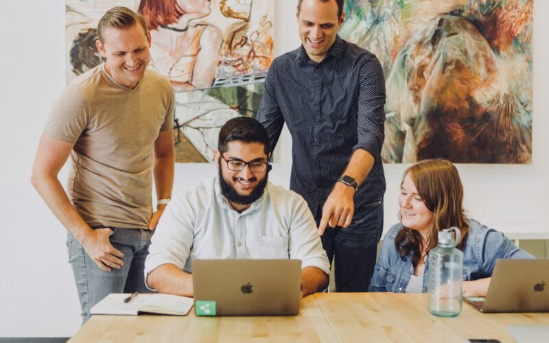 A small team smiling together around a laptop in a bright office.