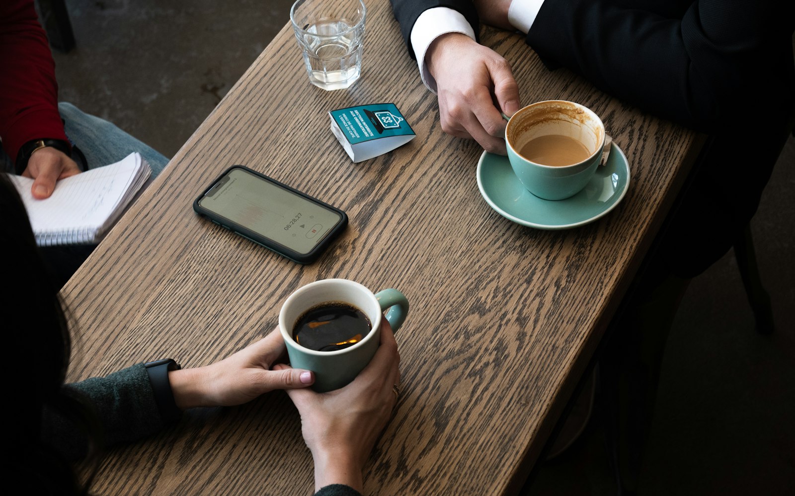 Two people talking over coffee at a wooden cafe table.