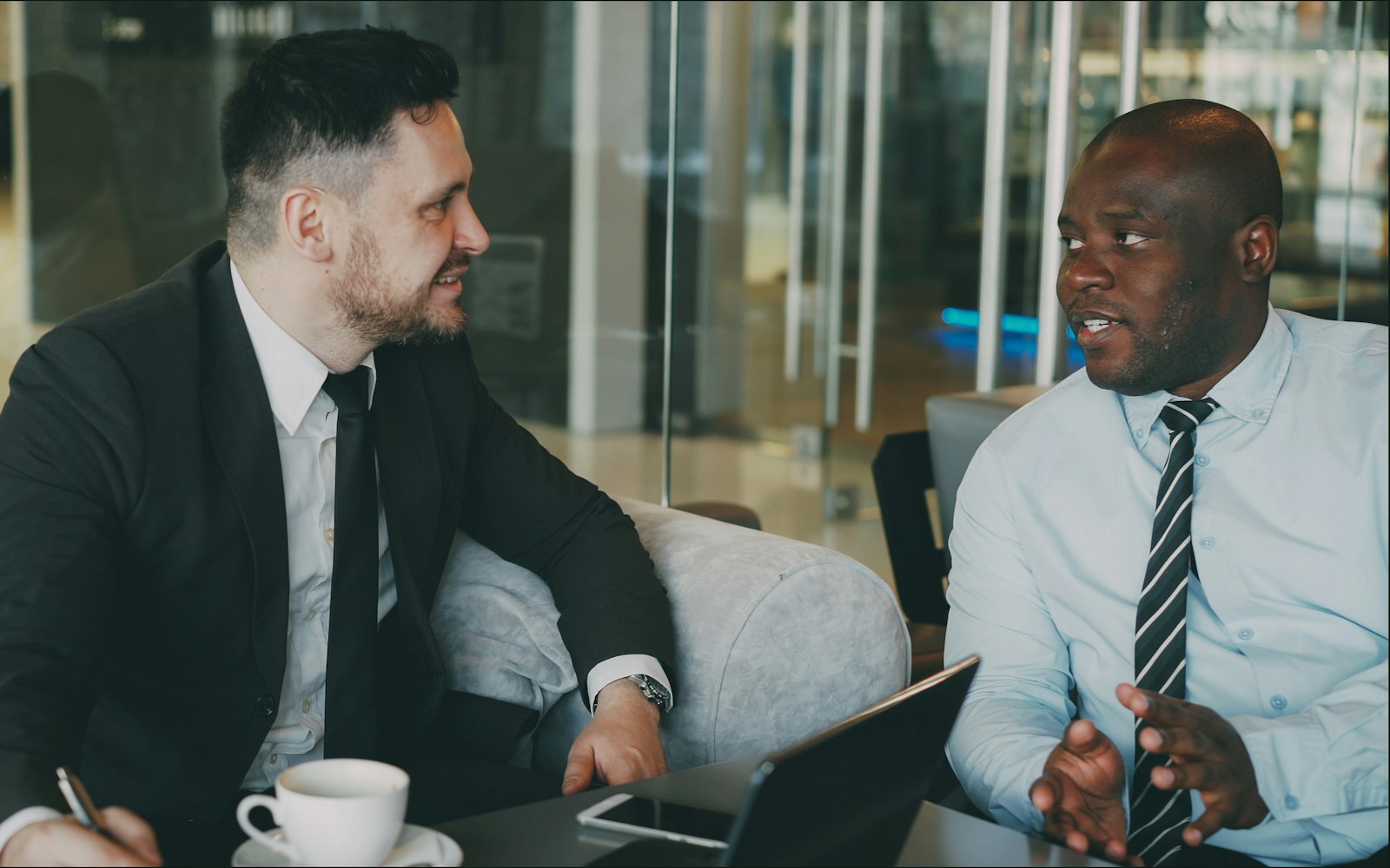 Two colleagues talking over coffee at a table in a bright office.